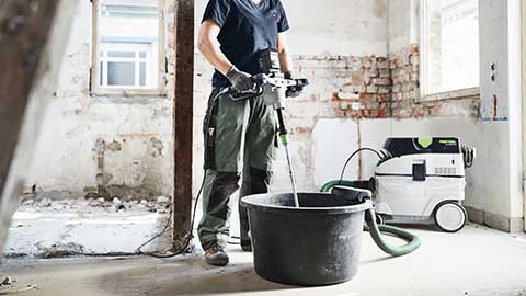 Una profesional está en una obra y utiliza un mezclador Festool en combinación con un aspirador.